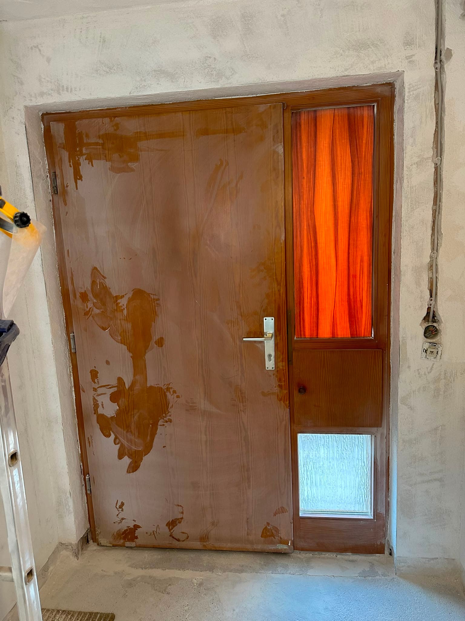 Vorher: alte braune Holztür mit orangefarbenem Vorhang im Glas-Seitenteil während der Sanierung